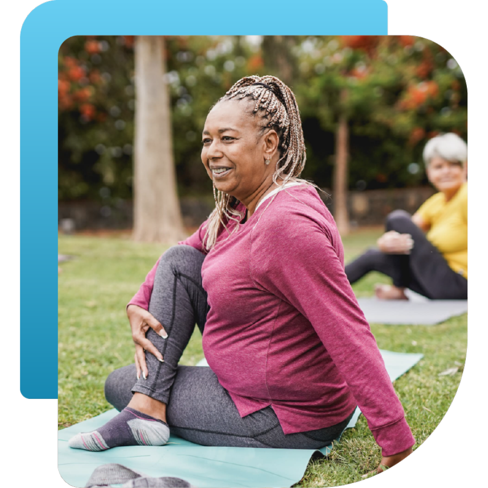 Smiling woman in activewear doing seated yoga stretches outdoors, promoting cancer wellness and survivorship programs